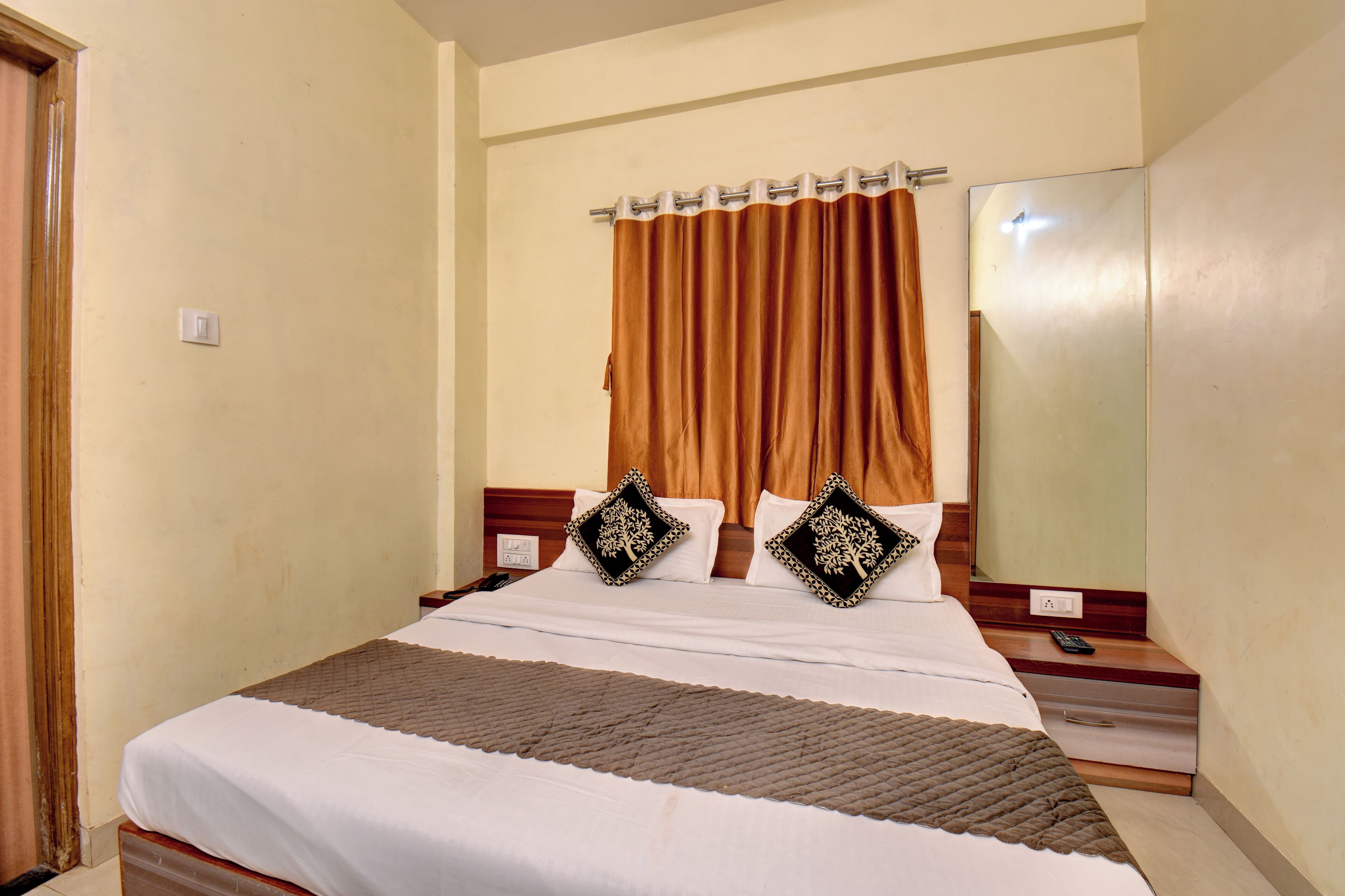 Ein Hotelzimmer mit Bett, Nachttisch, Spiegel und Vorhang.