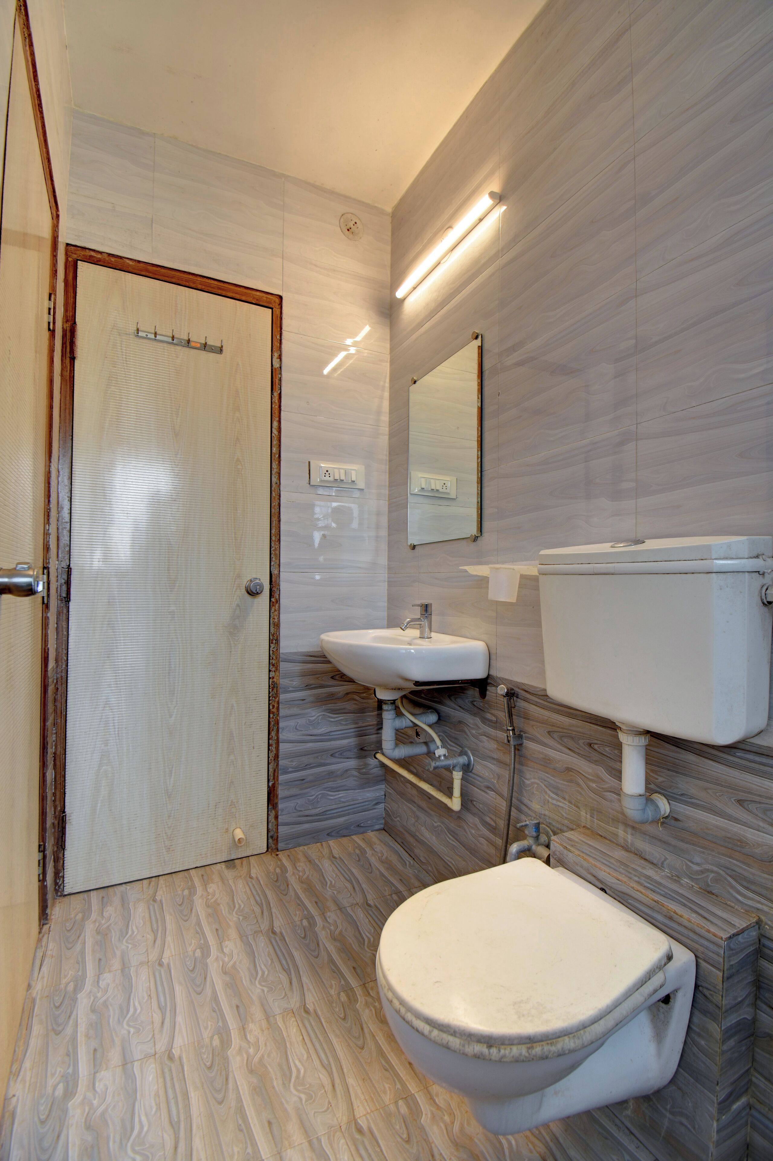 Un baño con suelo de madera, inodoro blanco, lavamanos y espejo.