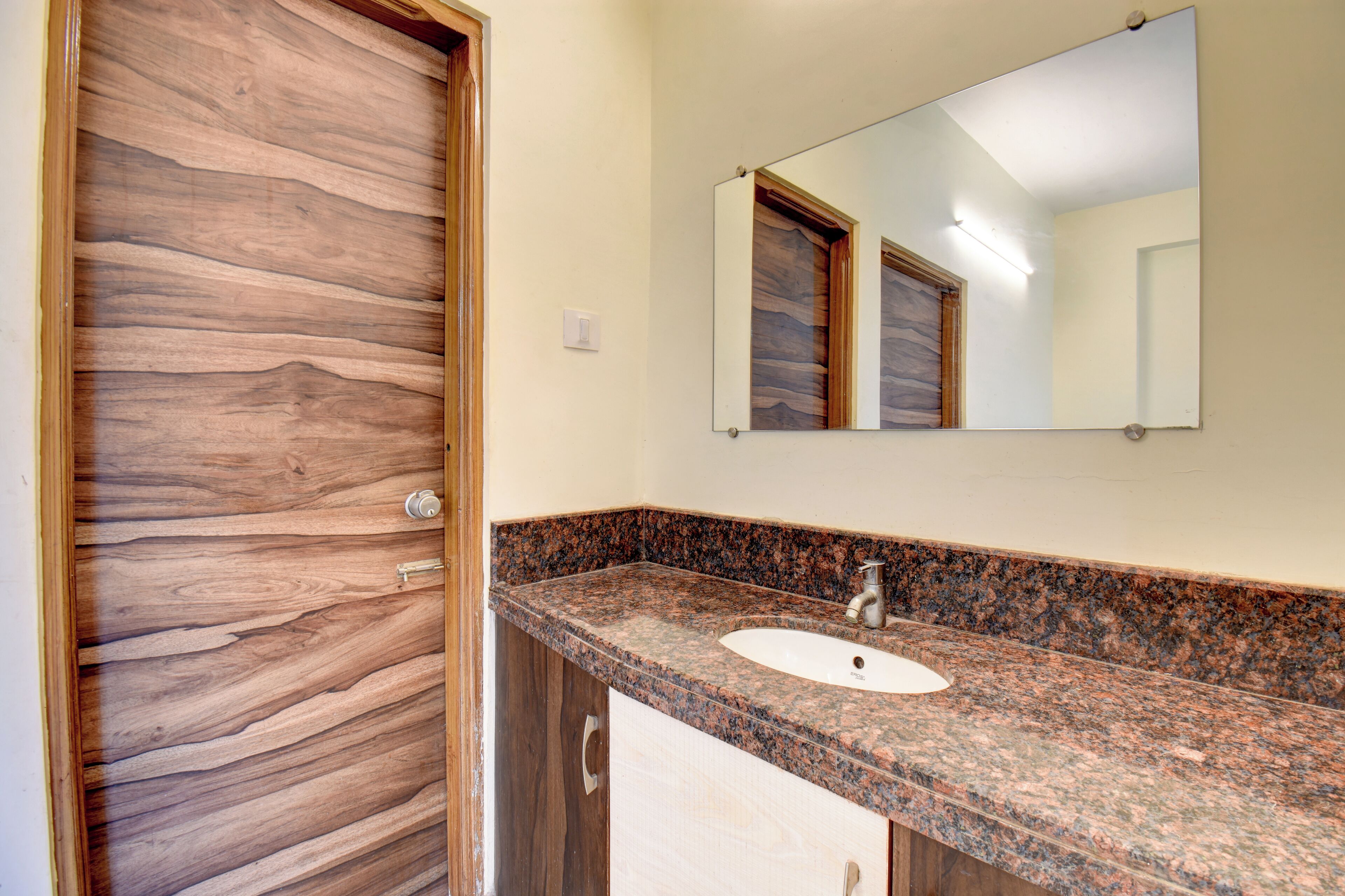 A bathroom with a wooden door, a granite countertop, a sink, and a mirror.