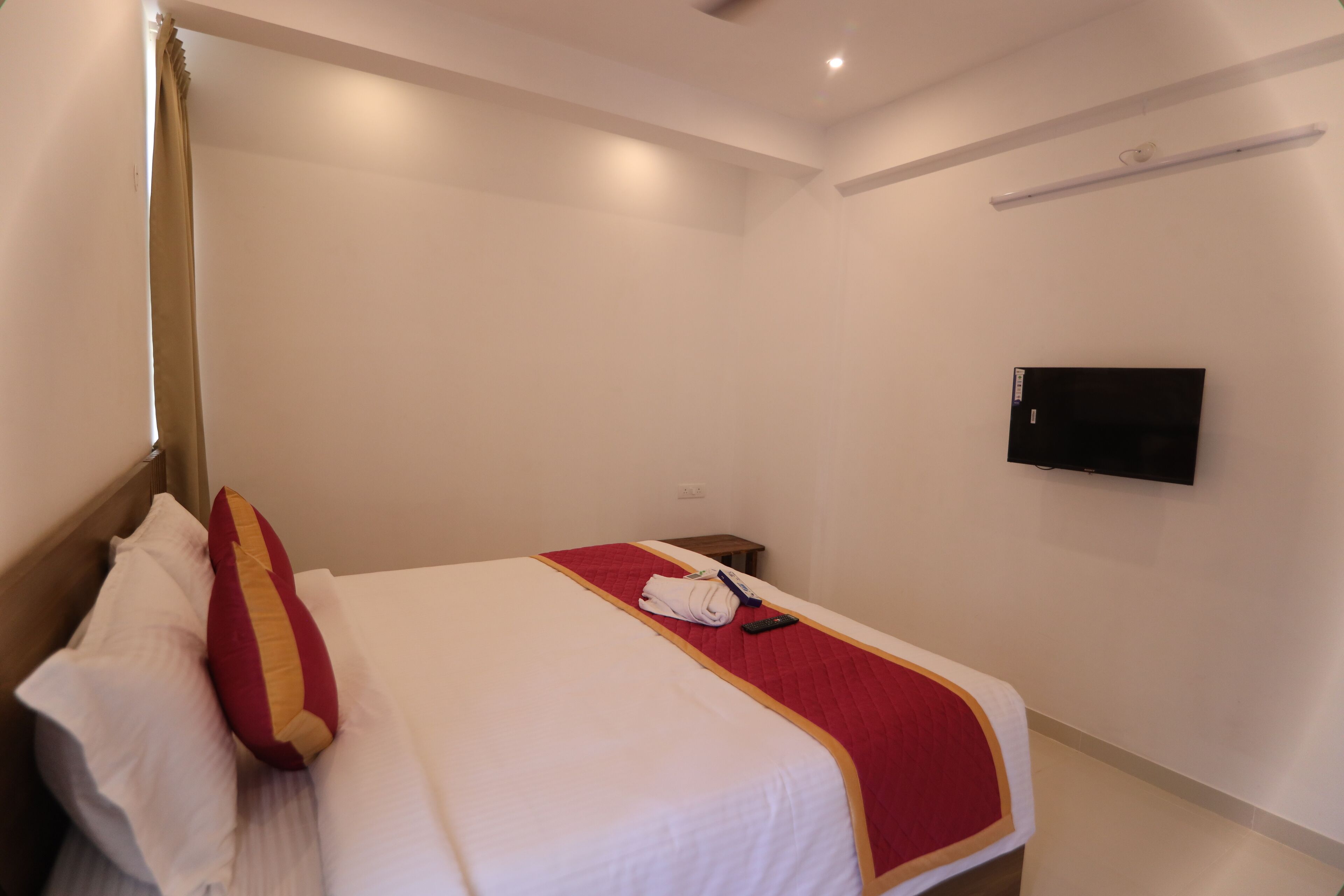 Ein Hotelzimmer mit einem ordentlich bezogenen Bett, einem an der Wand befestigten Flachbildfernseher und einem kleinen Nachttisch.