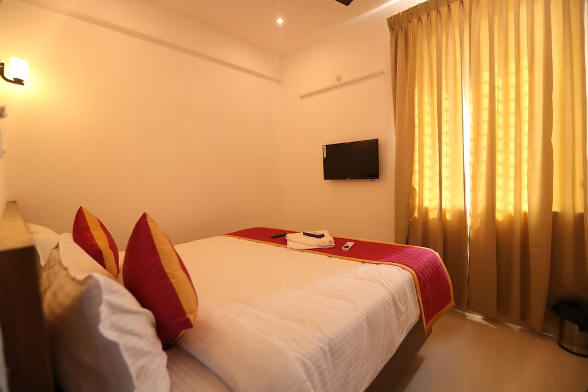 Een hotelkamer met een bed, kussens, een televisie en gordijnen.