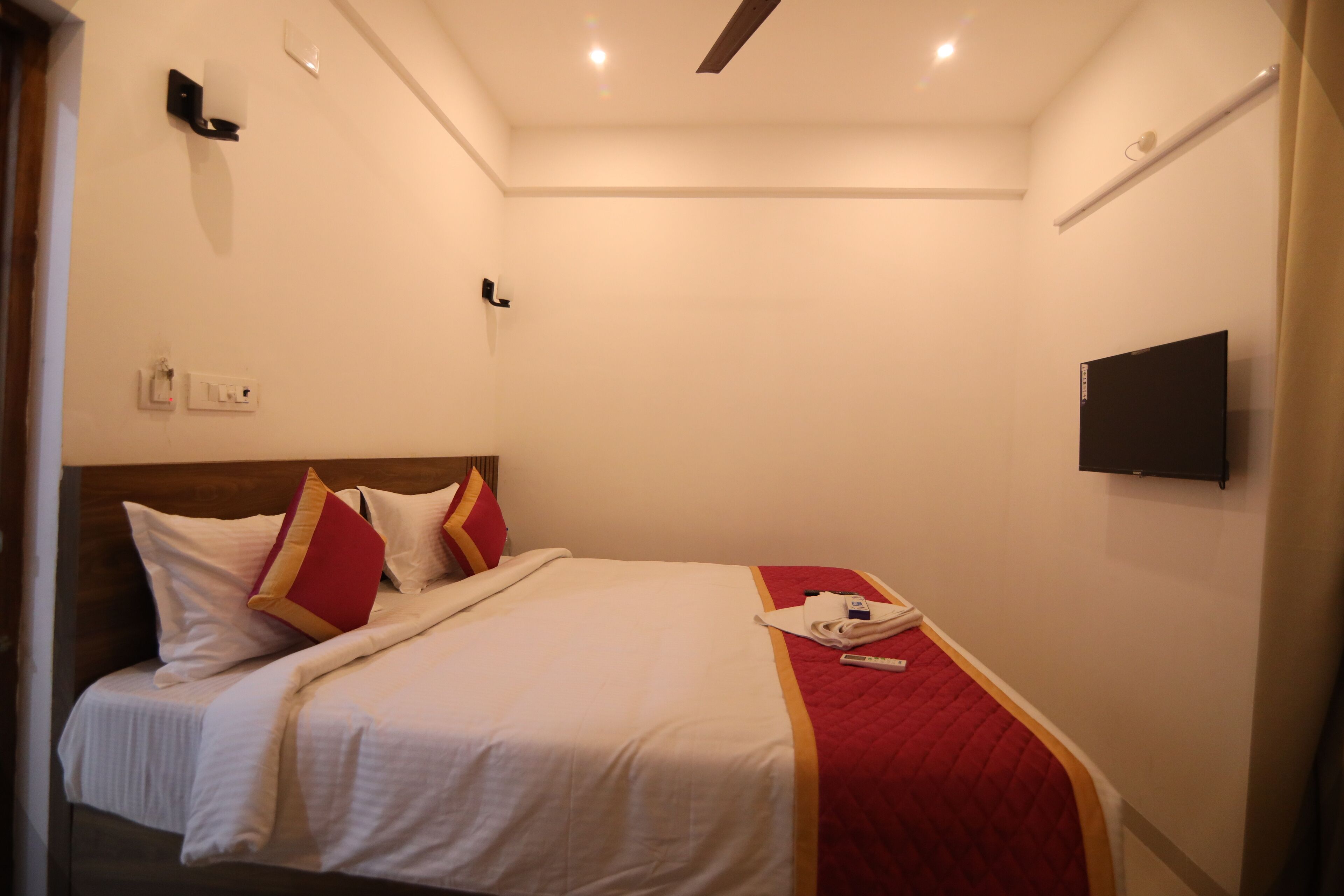 Een hotelkamer met een bed, een flatscreen televisie aan de muur en een rode accentkleur op het beddegoed.