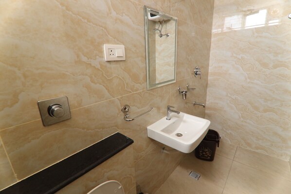 Un baño con pared de mármol, un lavamanos, un espejo, una ducha y un perchero para toallas.