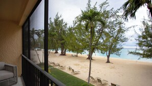 A balcony with a view of a beach, featuring lounge chairs and a palm tree. - Beachfront Bliss: Ground Floor Condo at The Islands Club, 7 Mile Beach, #05 (Grand Cayman)