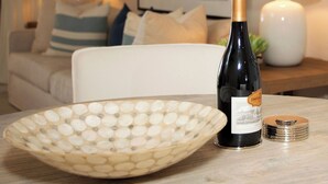 A living room with a white sofa, a decorative plate, a wine bottle, and a lamp on a wooden table. - Beachfront Bliss: Ground Floor Condo at The Islands Club, 7 Mile Beach, #05 (Grand Cayman)