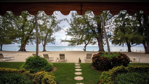 A beach view with a pathway leading to beach chairs and a small table. - Beachfront Bliss: Ground Floor Condo at The Islands Club, 7 Mile Beach, #05 (Grand Cayman)