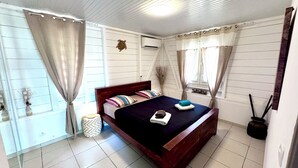 Un dormitorio con cama de madera, paredes blancas y suelo de baldosas.