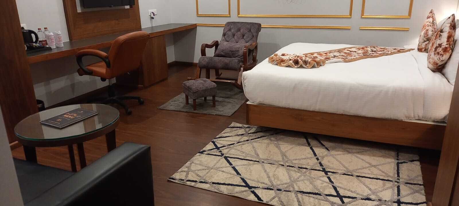 A hotel room with a bed, a desk, an office chair, a small round table, and a patterned rug.
