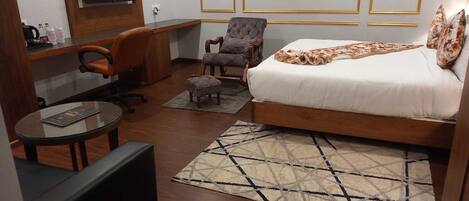 A hotel room with a bed, a desk, an office chair, a small round table, and a patterned rug.