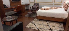 A hotel room with a bed, a desk, an office chair, a small round table, and a patterned rug. - Hotel Park Square  (Purnia)
