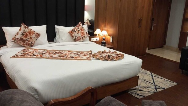 A hotel room with a large bed, a wooden wardrobe, a desk with a lamp, a sofa, and a chair. - Hotel Park Square  (Purnia)