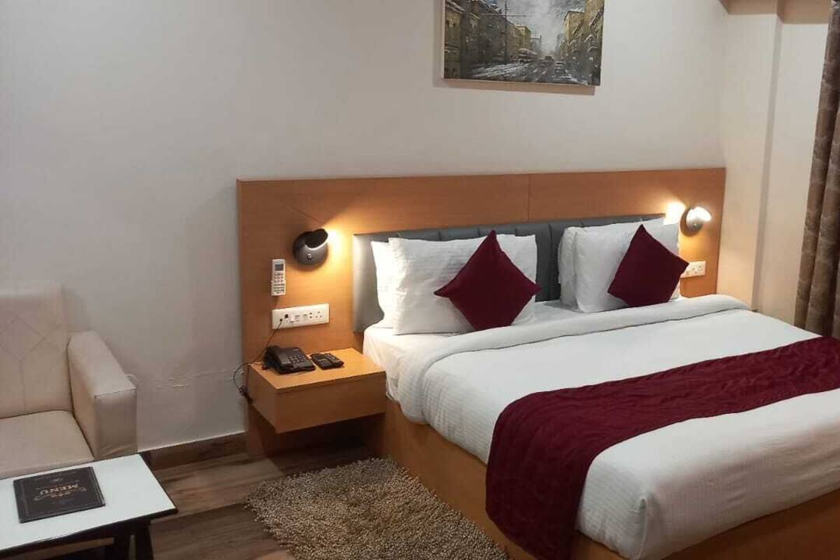 A hotel room with a bed, nightstand, lamp, and a painting on the wall.