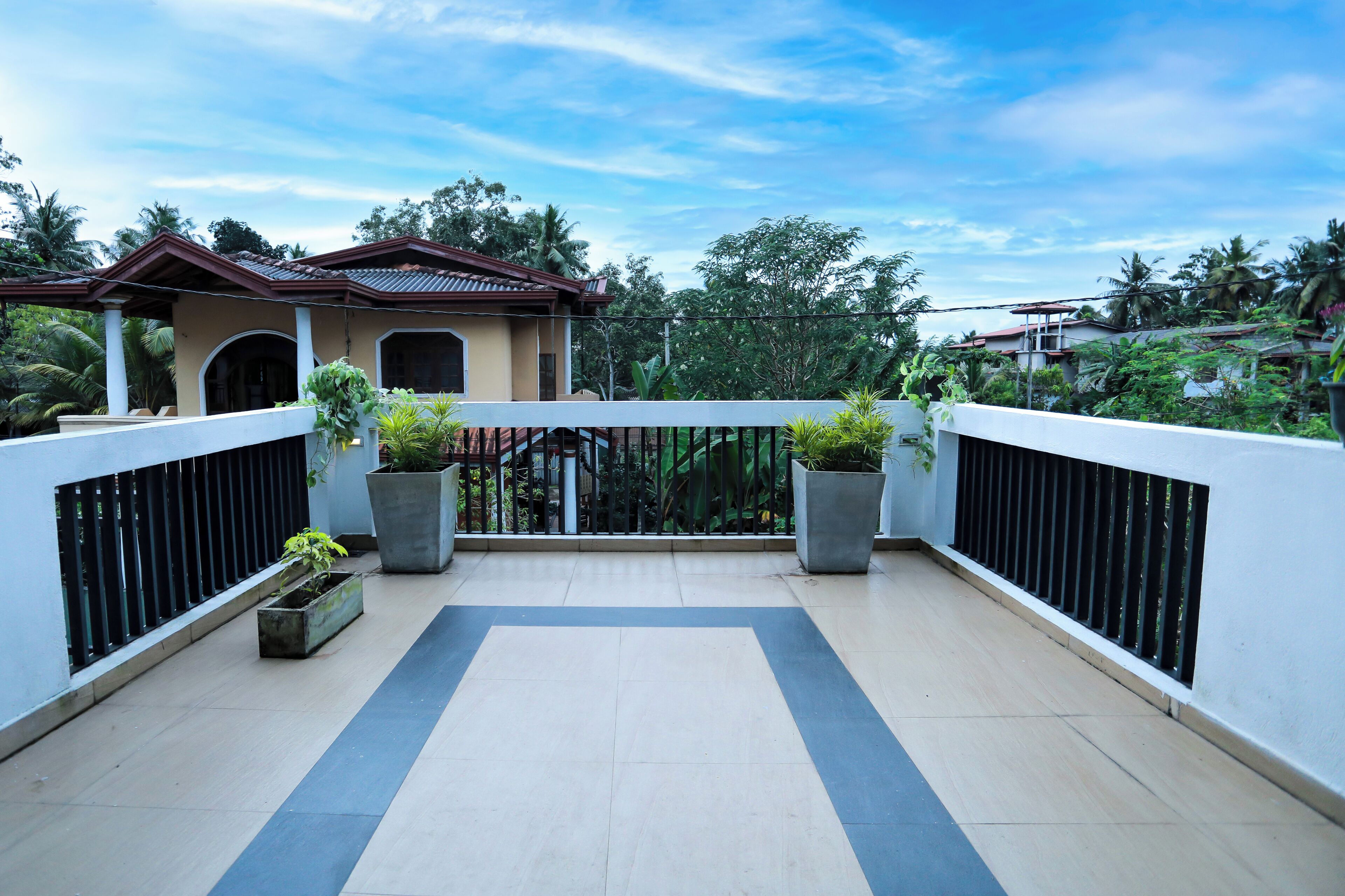 A balcony with a tiled floor, potted plants, and a view of a building with a tiled roof.