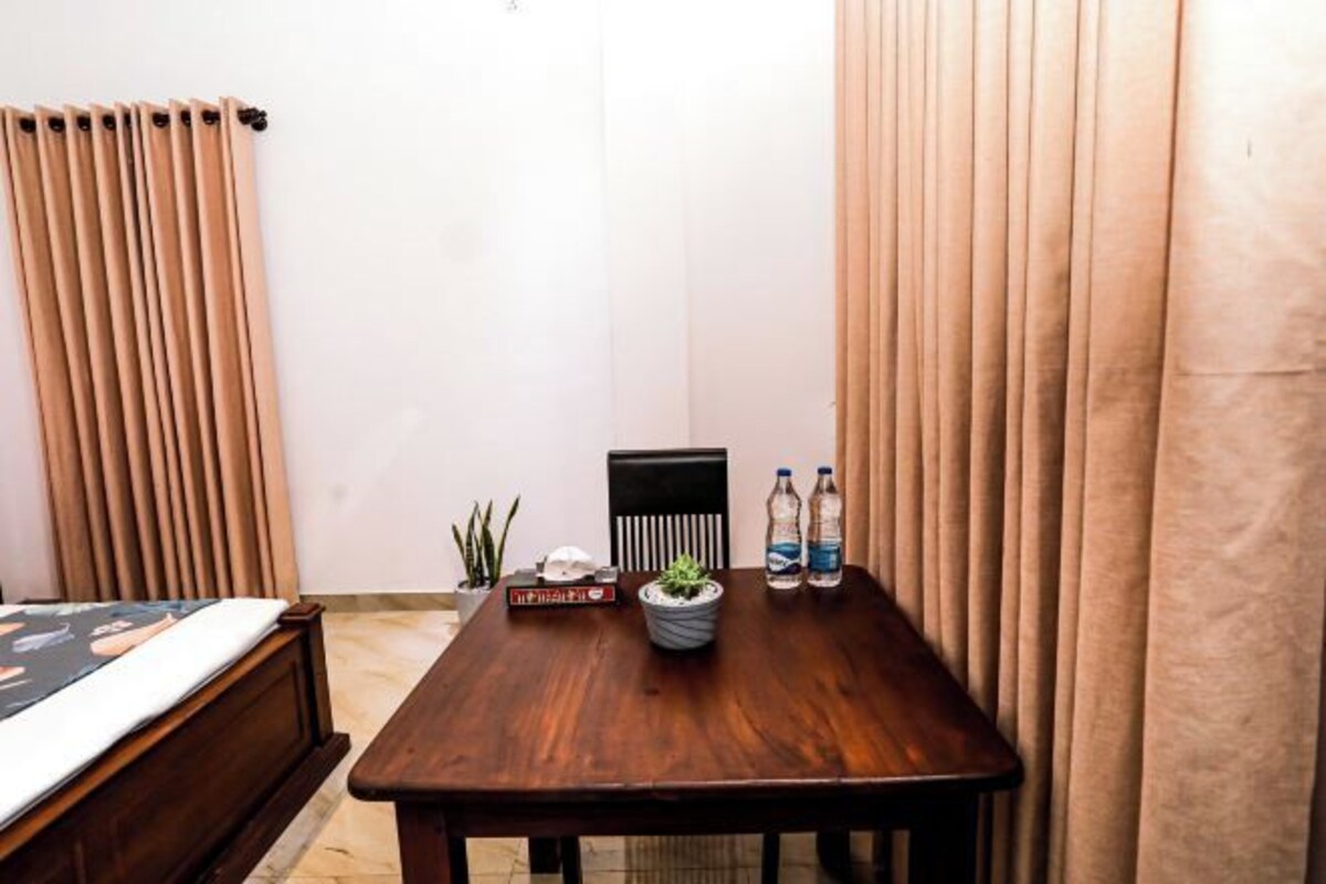 Una habitación con una cama de madera, una mesita con una planta en maceta, dos botellas de agua y una silla.