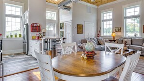 A spacious living area with a wooden ceiling, large windows, a dining table with chairs, and a cozy seating area with a sofa and cushions. - West Lafayette Home ~ 3 Mi to Purdue Campus! (West Lafayette)