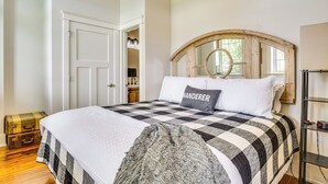 A bedroom with a checkered bedspread, a wooden headboard with a mirror, a suitcase, and a wardrobe with a mirror. - West Lafayette Home ~ 3 Mi to Purdue Campus! (West Lafayette)