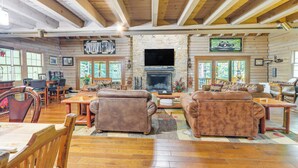 Ein geräumiges Wohnzimmer mit Holzböden, Ledersofas, einem Steinkamin und einem darüber montierten Fernseher.