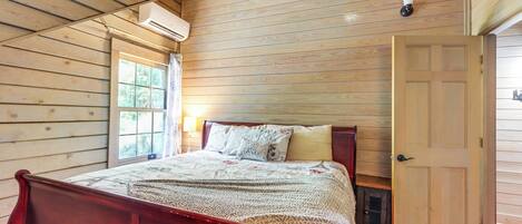 Un dormitorio con paneles de madera, una cama, una puerta y un equipo de aire acondicionado.