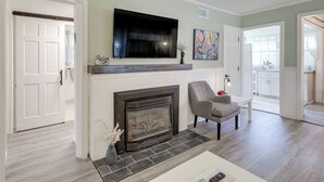 A living room with a fireplace, a mounted TV, and a chair. - < 2 Mi to Beach: Cozy Cottage w/ Patio on Cape Cod (Hyannis)