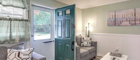 A living room with a teal door, a gray sofa, a white side table, and a wall art piece.