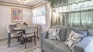 A dining area with a table and chairs, a sofa with patterned cushions, and a window with floral curtains. - < 2 Mi to Beach: Cozy Cottage w/ Patio on Cape Cod (Hyannis)