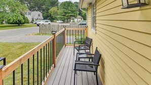A wooden deck with chairs and a railing, a yellow house, and parked cars in the background. - < 2 Mi to Beach: Cozy Cottage w/ Patio on Cape Cod (Hyannis)