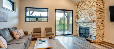 A spacious living room with a stone fireplace, a large window, and a ceiling fan.