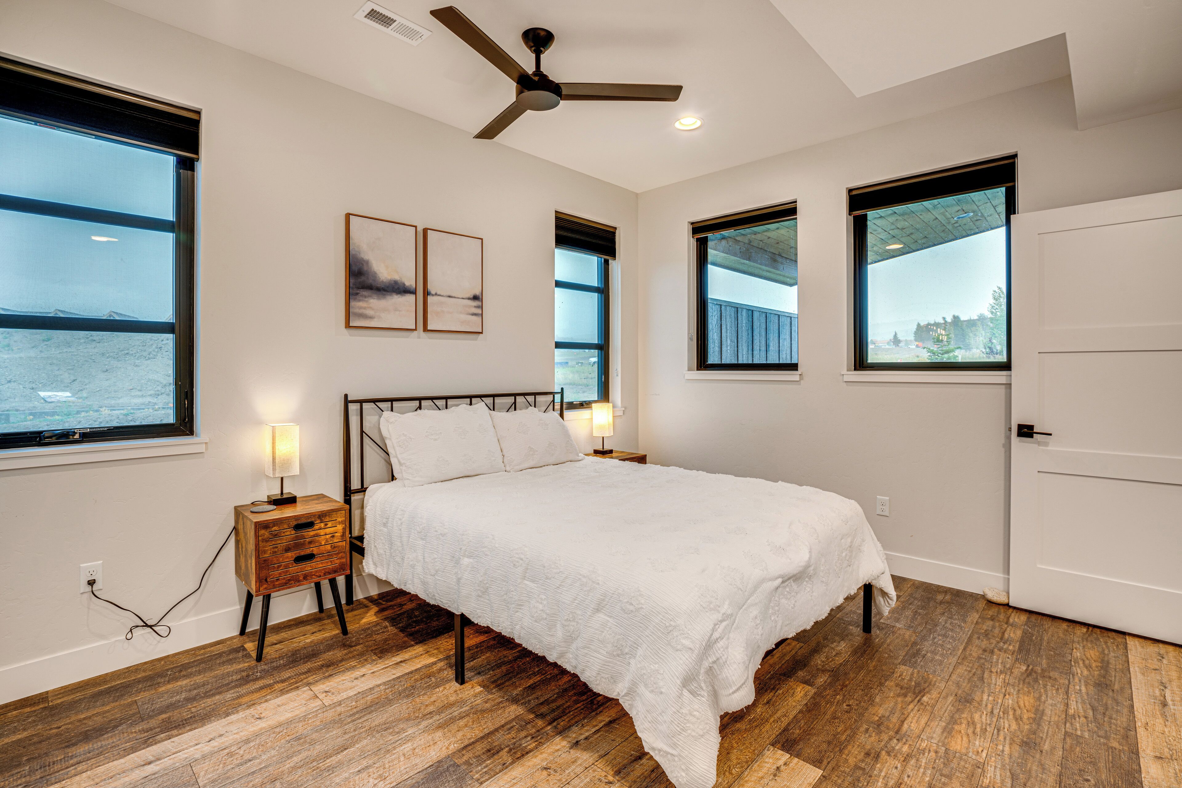 A bedroom with a bed, bedside tables, a ceiling fan, and large windows with views.