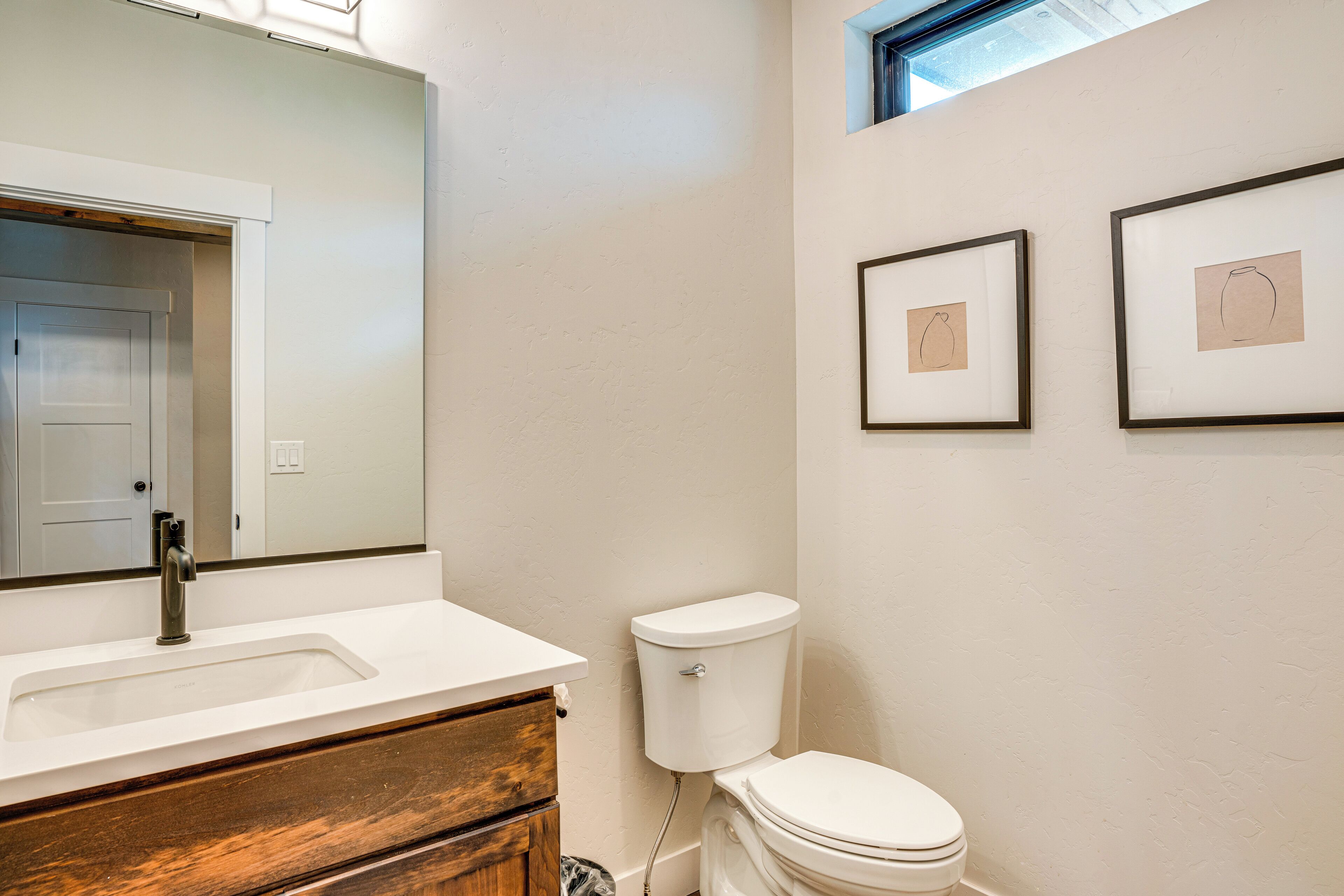 A bathroom with a white sink, wooden vanity, white toilet, and two framed drawings on the wall.
