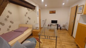 Una habitación pequeña con cama, una mesita, televisor y armario.