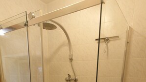 Cabina de ducha con paredes de vidrio, un cabezal de ducha de mano y un grifo empotrado.