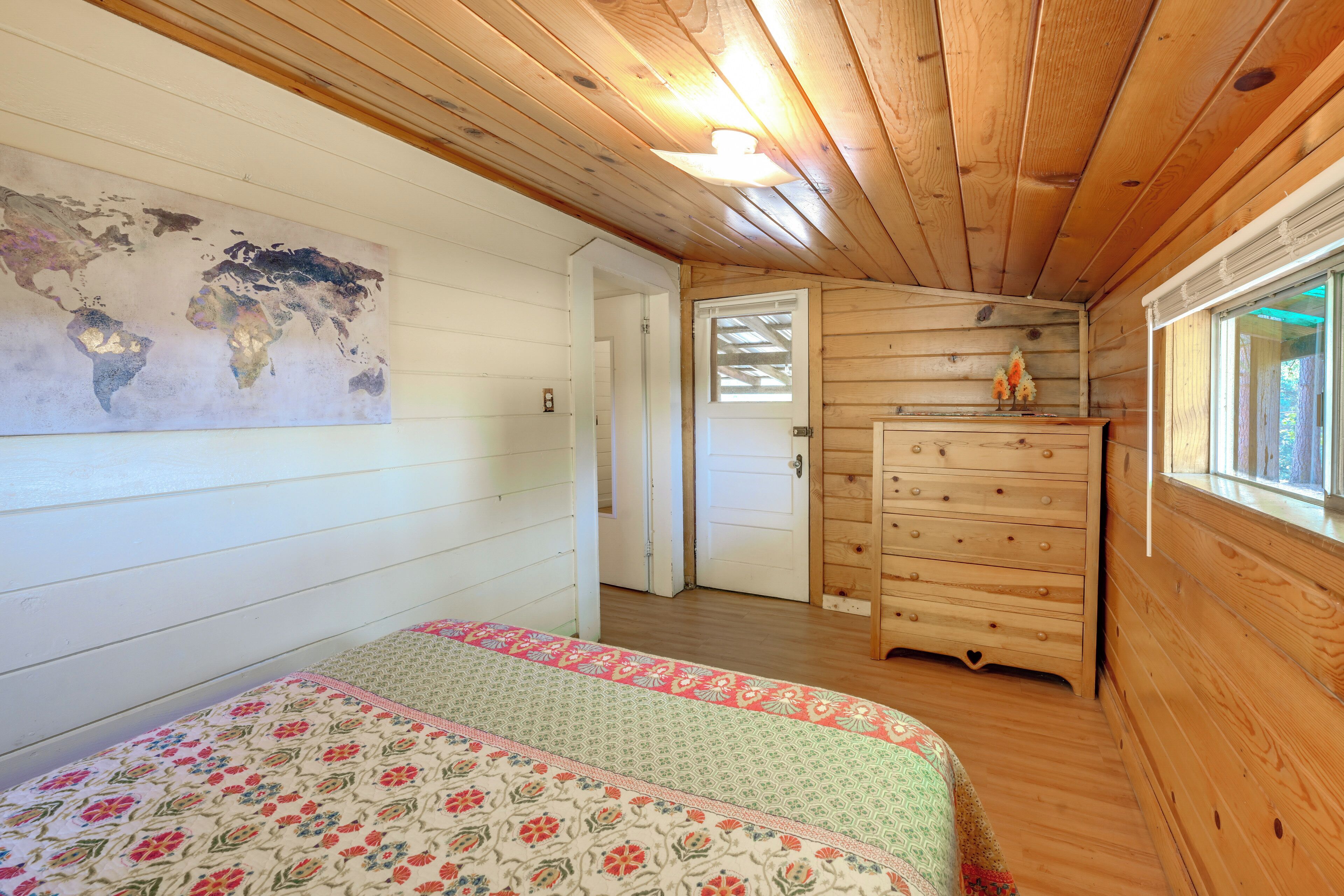 A wooden cabin room with a bed, dresser, and a world map on the wall.