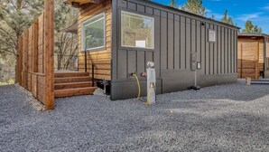 A compact, single-story RV with a wooden exterior and large windows, equipped with a water heater and a hose.