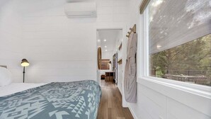 Un dormitorio con cama, lámpara, ventana con cortinas y vistas a árboles.