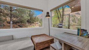 Habitación con vistas a un paisaje montañoso, un escritorio de madera, un banco y una lámpara.
