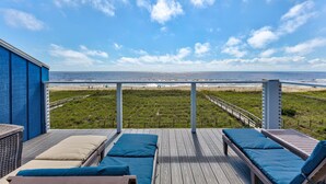 A deck with lounge chairs overlooking a beach and ocean.