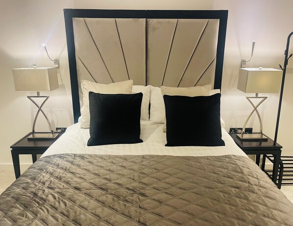 A neatly made bed with a quilted headboard, two bedside tables with lamps, and a view of the room's architecture. - St Albans City Retreat - 2 Bed Apartment (St Albans)
