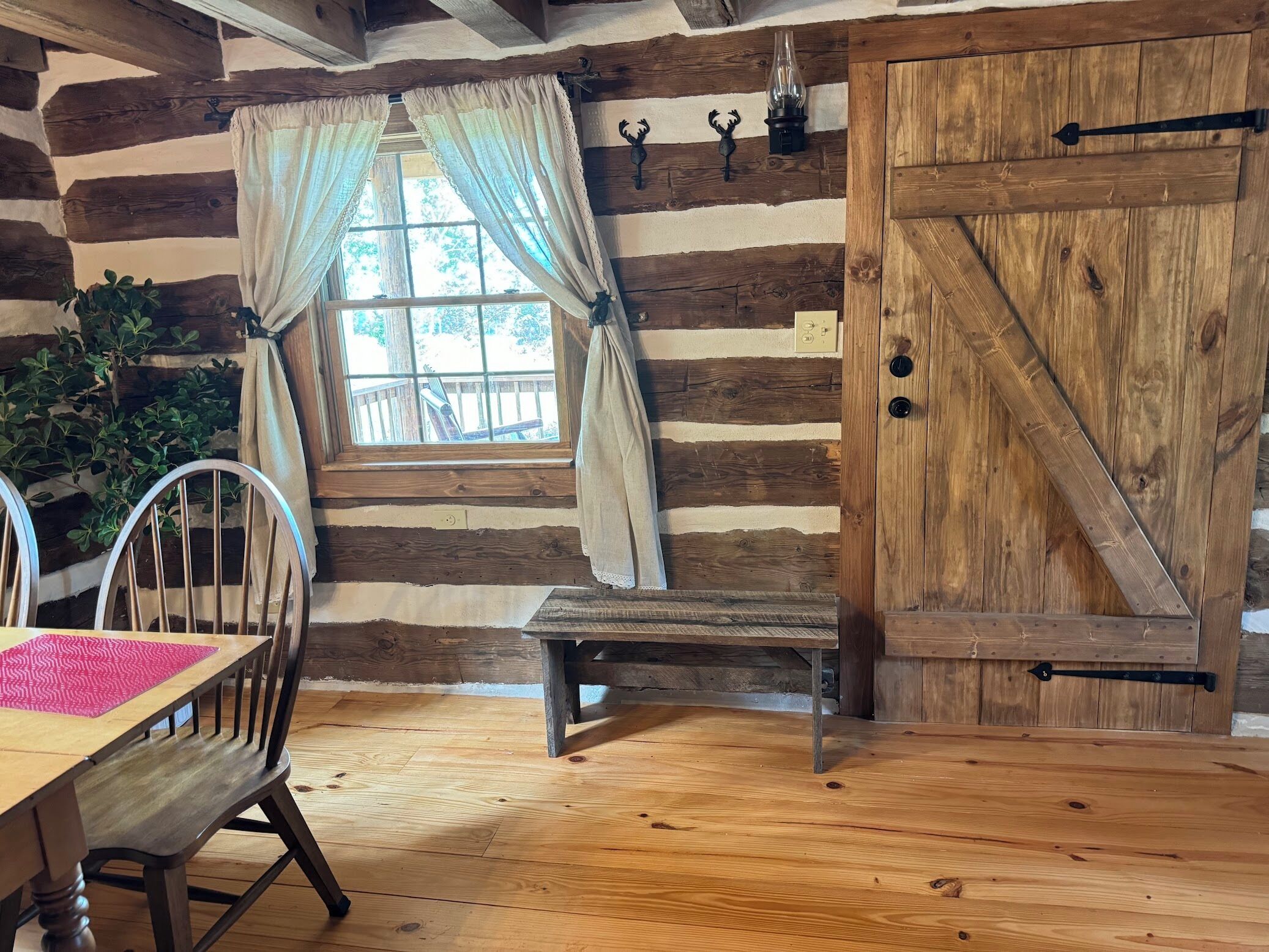 Interior rústico de una cabaña con una mesa de madera, un banco y una puerta grande de madera.