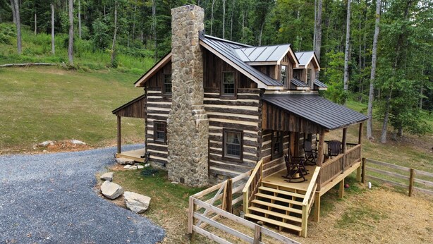A log cabin with a stone chimney, a porch with seating, and a view of the surrounding forest. - Log cabin with mountain VIEWS in Lexington! Near VA Horse Ctr, 8 mi from VMI/W&L (Lexington)
