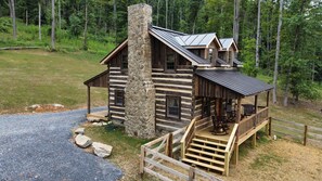 Una cabana de fusta amb una xemeneia de pedra, un porxo amb seients i una vista del bosc circumdant.