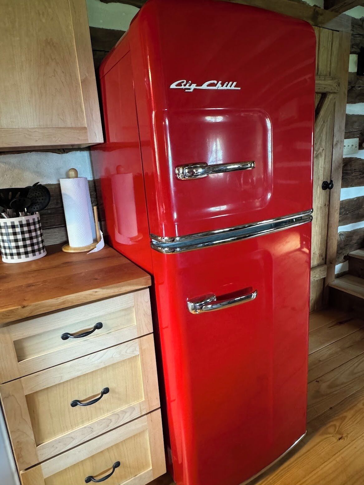 A red kitchen with a vintage refrigerator, wooden cabinets, and a checkered mug on the counter.