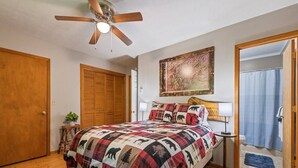 A bedroom with a bed, a ceiling fan, a painting, a door, and a bathroom visible through an open door. - Sunset Creek-Pets Welcome, Motorcycle Friendly (Maggie Valley)