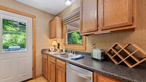 A compact kitchen with wooden cabinets, a granite countertop, a dishwasher, and a wine rack. - Sunset Creek-Pets Welcome, Motorcycle Friendly (Maggie Valley)