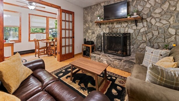 A living room with a stone fireplace, leather sofa, and a television mounted on a stone wall. - Sunset Creek-Pets Welcome, Motorcycle Friendly (Maggie Valley)