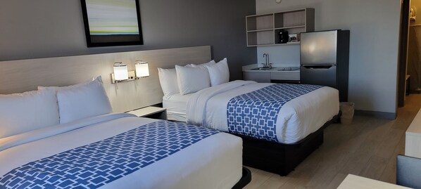 Une chambre d’hôtel avec deux lits, une petite kitchenette et un téléviseur fixé au mur.