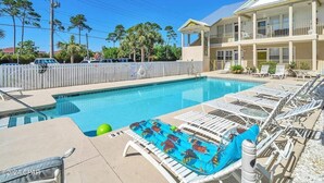 A pool area with lounge chairs, a pool, and a building with a balcony.