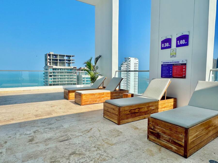 A rooftop lounge with wooden furniture, a view of the city, and a sign indicating a 1.40MTS fee.