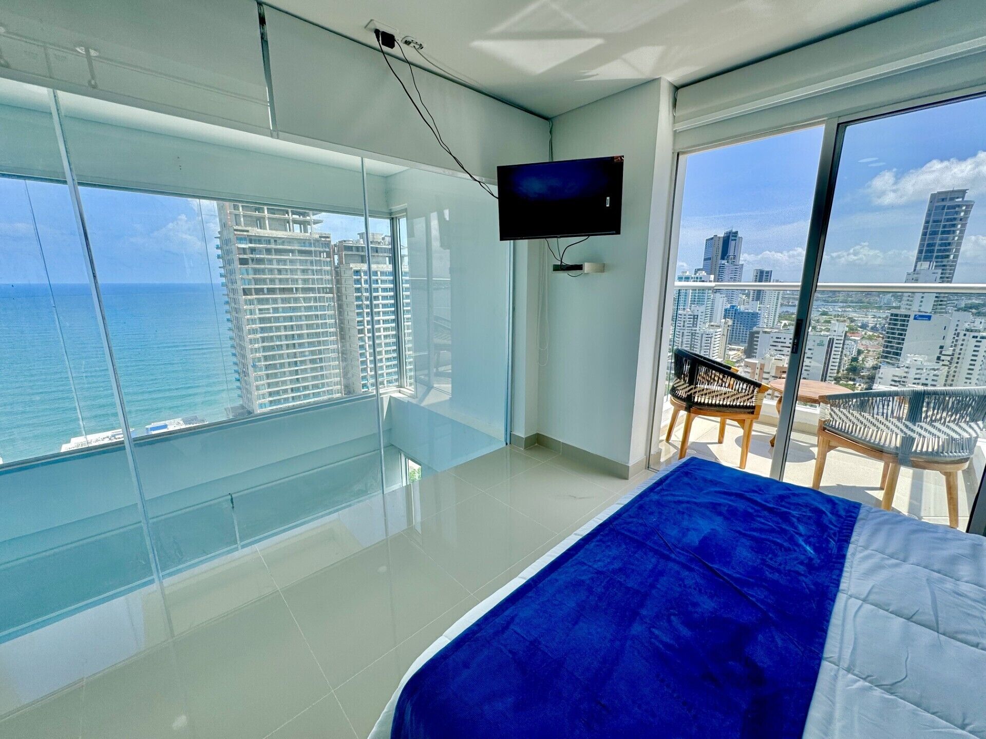 Quarto moderno com uma janela grande, televisão de tela plana e varanda com vista para a cidade.