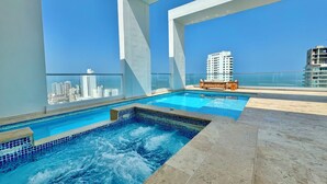 A rooftop pool with clear blue water, a wooden bench, and a city view. - Apartamento Navy 2 habitaciones (Cartagena)