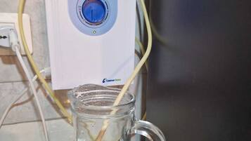 A clear glass pitcher with a handle, connected to a white device with a blue dial, possibly a water filter or purifier, on a countertop.